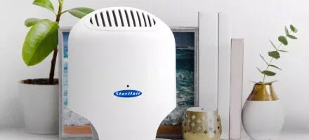 Purificador de ar Sterilair branco em uma estante, entre plantas e livros